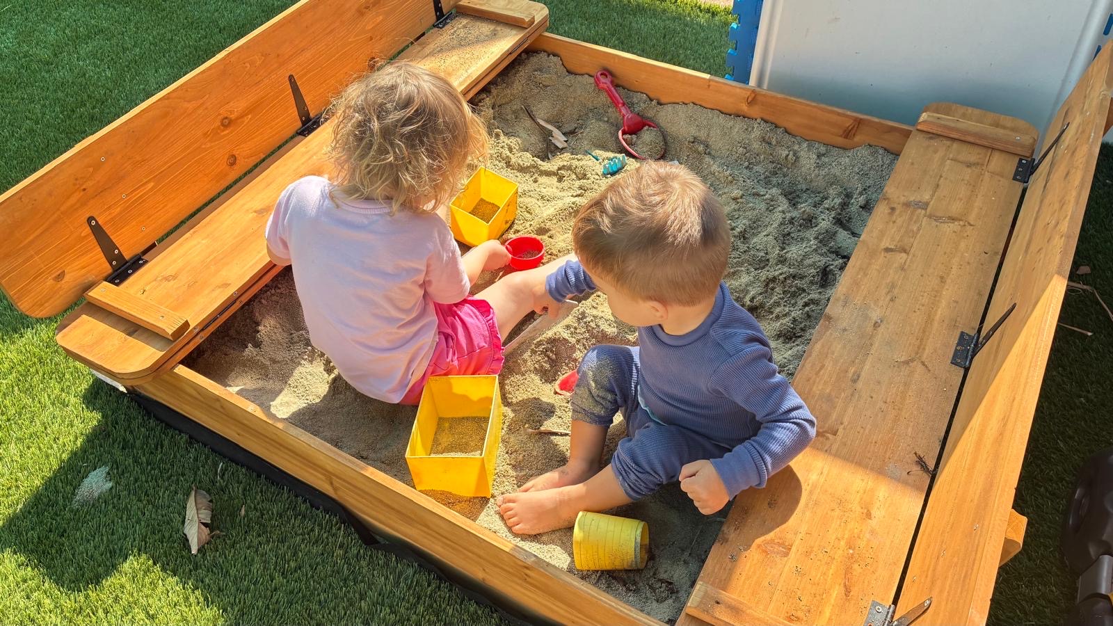 Children playing together in a wooden sandbox in the daycare yard